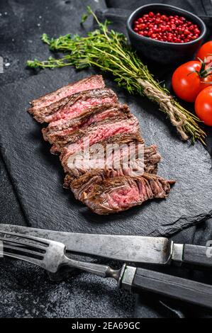 Steak de flanc en tranches grillé avec assaisonnements et épices. Arrière-plan noir. Vue de dessus Banque D'Images