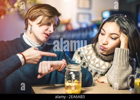 Deux femmes mécontentes sont fatiguées d'attendre leur commande dans un restaurant ou un bar et pointent vers l'horloge. Le concept de service de mauvaise qualité par un WAI Banque D'Images
