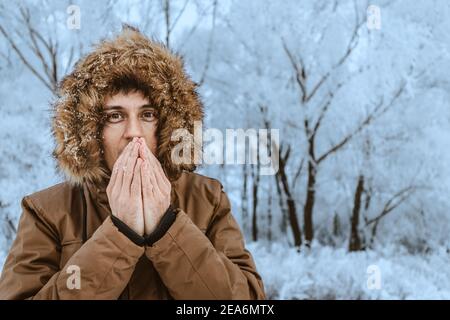 Un homme gèle dans le froid de la forêt et essaie de se passer les mains de son souffle. Le concept de gelure des extrémités et d'hypothermie de la TH Banque D'Images