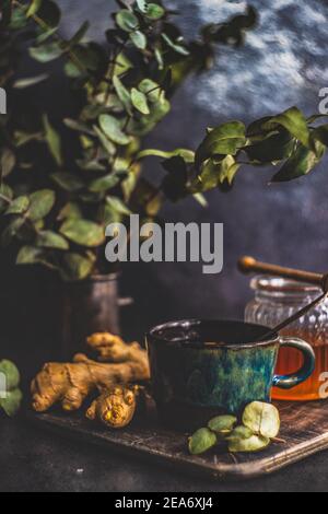 Tasse de thé chaud avec miel, citron et gingembre à côté des tiges d'eucalyptus dans un vase Banque D'Images