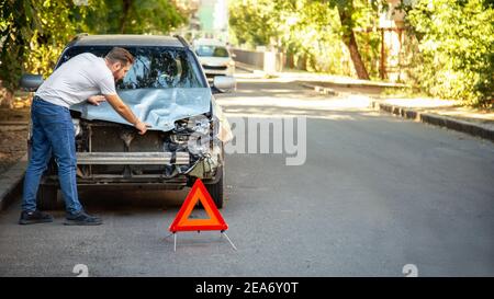 Conducteur regardant sur une voiture de naufrage dans un accident de voiture. L'homme regrette de réparer les phares de la voiture après un accident de voiture. Collision avec une voiture tragique. Trajet dangereux Banque D'Images