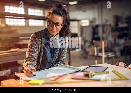 Concepteur créatif d'âge moyen dans son studio de fabrication faisant à travers des plans papier. Travail nocturne. Banque D'Images