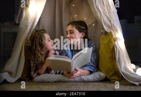 Sœurs à l'intérieur à la maison, lisant le livre en pyjama. Concept de verrouillage. Banque D'Images