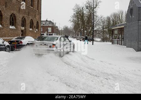 ZUTPHEN, PAYS-BAS - 07 février 2021 : éclaboussures de neige derrière une voiture qui roule dans des rues blanches glissantes après de fortes chutes de neige Banque D'Images