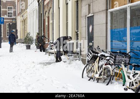 ZUTPHEN, PAYS-BAS - 07 févr. 2021: Les voisins hollandais en centre-ville nettoient manuellement le porche avant avec une pelle après de fortes chutes de neige Banque D'Images
