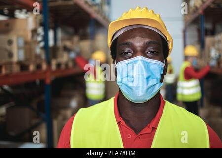 Travailleur africain regardant la caméra à l'intérieur de l'entrepôt tout en utilisant Masque de sécurité - attention au visage Banque D'Images