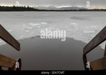 Trou dans la glace pour se baigner près du nez en bois sur gelé lac en haute-Bavière avec Alpes en arrière-plan en hiver avec de la neige Banque D'Images