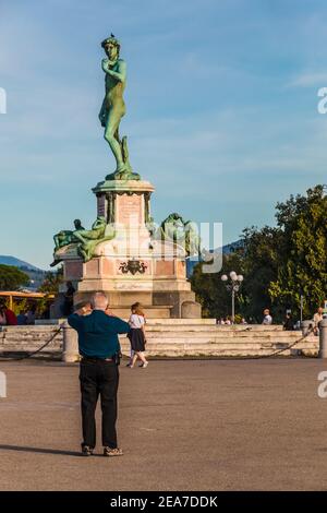 Vue magnifique sur un vieil homme prenant une photo d'une réplique en bronze d'un David de Michel-Ange au centre de la place Piazzale Michelangelo, situé... Banque D'Images