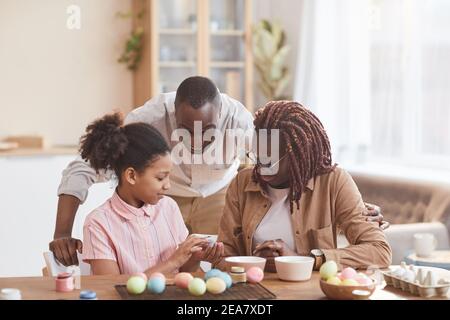 Portrait d'une famille afro-américaine aimante peignant des œufs de Pâques ensemble tout en étant assis à une table en bois dans un intérieur confortable et en appréciant l'art du bricolage, cop Banque D'Images