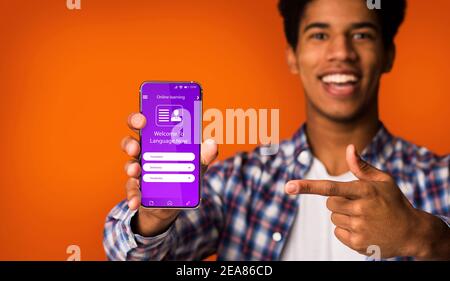 Happy Black Guy pointant vers un smartphone avec une application ouverte pour Formation en ligne Banque D'Images