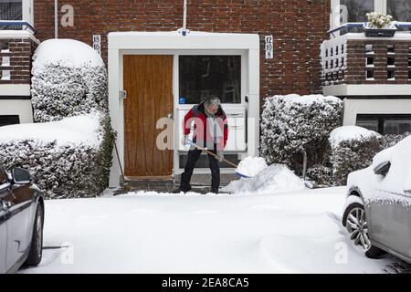 ZUTPHEN, PAYS-BAS - 07 février 2021 : résident nettoyant manuellement le porche avant avec une pelle après de fortes chutes de neige dans le quartier résidentiel néerlandais Banque D'Images