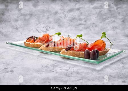trois bruschetta à la truite, au saumon, au fromage à la crème et au micro-vert sur une plaque de verre sur fond blanc Banque D'Images