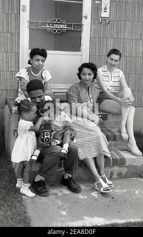 Les années 1960, Chicago, USA, une famille qui prend ses photos sur les marches de sa propriété, avec les deux plus jeunes filles qui s'intéressent à l'appareil photo de leur père, Ciroflex, un appareil photo reflex à deux objectifs (TLR). La société Ciro Camera a commencé à fabriquer des caméras à Detroit, en 1941, puis au Delaware, en Ohio, à partir de 1947. En 1951, Graflex a acquis les droits de fabriquer l'appareil photo et a produit le reflex à double objectif Ciro Flex. Six modèles ont été fabriqués, celui ici, le modèle E, était connu comme le 'travail de l'homme Rolleiflex', car il était abordable pour l'homme dans la rue. Banque D'Images