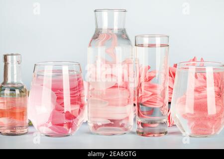 fleurs roses déformées par l'eau dans les verres et la bouteille sur fond bleu. Décoration maison, écologique, détente, concept de jardinage. Espace copie Banque D'Images