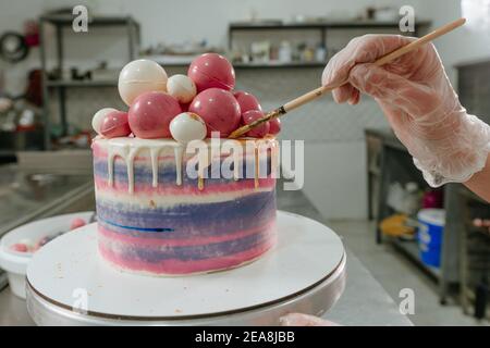 Gros plan de la confiserie féminine décorant le gâteau d'anniversaire à l'aide de comestible colorer et brosser d'or dans le studio de confiserie Banque D'Images