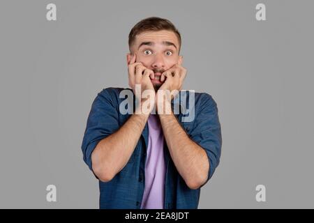 Un homme caucasien effrayé piquant ses ongles dans la terreur sur fond gris de studio. Exprimer le concept des émotions négatives Banque D'Images