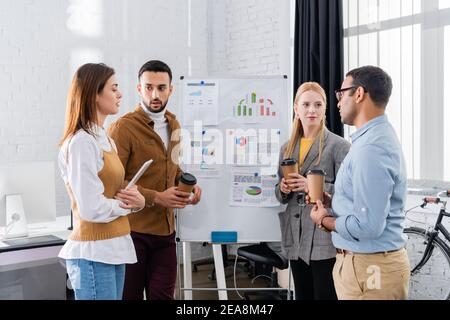 Professionnels multiethniques avec café à emporter et tablette numérique près du tableau de conférence Banque D'Images