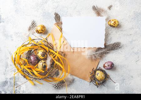 Œufs de caille de Pâques jaunes et violets colorés avec plumes dans de petits nids et carte de voeux dans l'enveloppe. Faible profondeur de champ. Vue de dessus. Espace pour te Banque D'Images