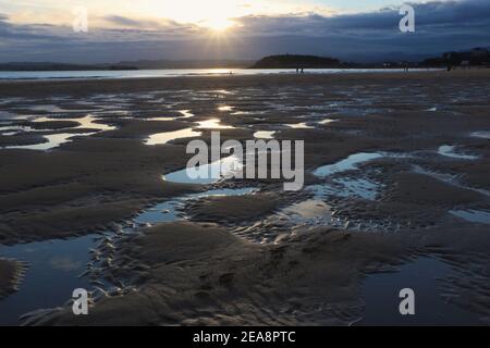 Personnes sur la plage à marée basse avec un modèle de sable et d'eau de mer avec le ciel reflété dans l'eau tôt le matin Santander Cantabria Espagne hiver Banque D'Images