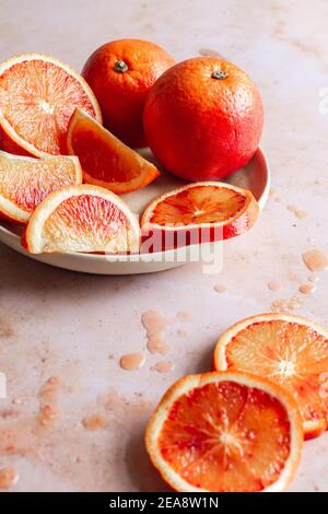 Assiette d'oranges de sang frais, un entier, un peu coupé en deux, tranché ou coupé en quartiers avec des gouttes de jus d'orange de sang sur le fond. Banque D'Images