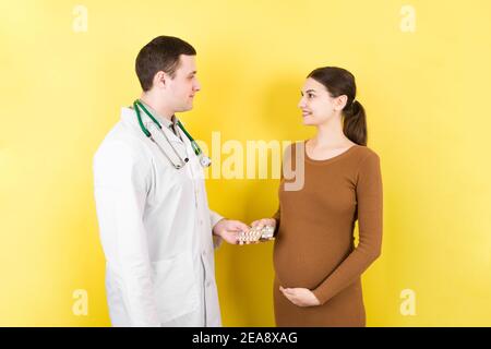 Pilules de gving de gynécologue mâle à la femme enceinte pendant le rendez-vous sur fond coloré. Visite à UN concept de soins de santé et de personnes de grossesse de docteur. Banque D'Images