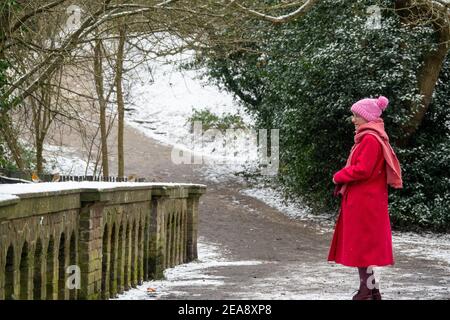 Une femme portant un manteau rouge et un chapeau de galet rose debout dans la neige observant robins et d'autres oiseaux sur Bird Bridge à Hampstead Heath, Londres, Royaume-Uni. Banque D'Images