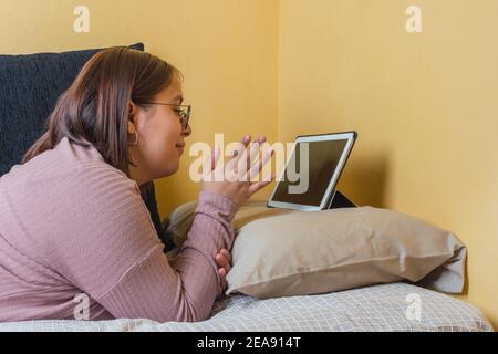 Femme latine effectuant un appel vidéo avec sa tablette écran noir étiré sur le lit Banque D'Images