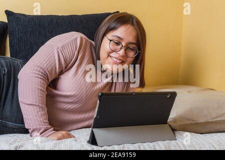 jeune fille regardant son écran de tablette souriant étiré sur le lit Banque D'Images