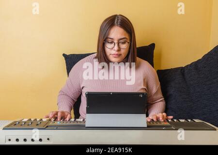 jeune fille assise avec des coussins jouant le piano avec un tablette Banque D'Images