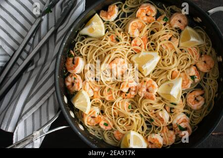 Pâtes de crevettes au beurre d'ail dans une sauteuse : crevettes et spaghetti dans une sauce au beurre d'ail et garnies de quartiers de citron Banque D'Images