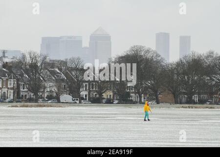 Un homme marche à travers un parc de Wanstead couvert de neige avec une toile de fond des gratte-ciels de l'île de Dogs. De fortes chutes de neige et de glace ont perturbé certaines parties du Royaume-Uni, Londres recevant environ 5 cm de neige. Les vents forts de l'est de la tempête Darcy ont plongé les températures dans certaines parties du Royaume-Uni en dessous de moins un. Banque D'Images
