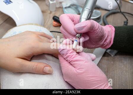 Enlever l'ancien ongle hybride à l'aide d'une meuleuse électrique, l'esthéticienne a des gants en latex rose. Banque D'Images