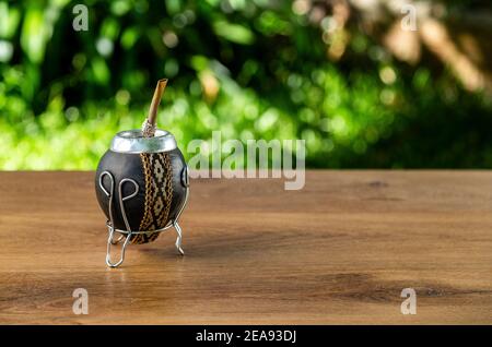 Traditionnel Argentin Mate fait de potiron et doublé en cuir sur une table en bois en plein air. Arrière-plan vert flou. Banque D'Images