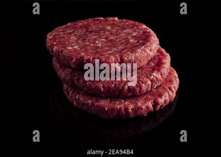 Gros plan d'une pile de patties hamburger crues sur une surface noire Banque D'Images