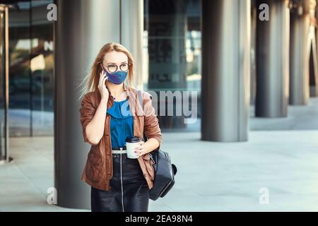 Femme portant un masque facial parlant au téléphone à l'extérieur pendant les déplacements Banque D'Images