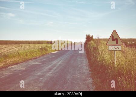 Image dans les tons rétro d'une route de campagne au coucher du soleil, en Pologne. Banque D'Images