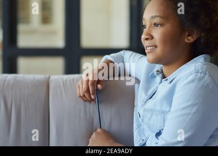 Portrait d'une jeune fille en train de faire des devoirs, assise sur le canapé à la maison Banque D'Images