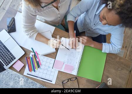 Vue de dessus de la race mixte de l'adolescence fille faisant des tâches mathématiques, devoirs d'école avec une enseignante dans le salon à la maison Banque D'Images