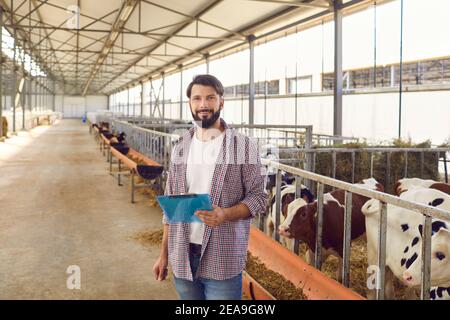 Propriétaire de ferme avec un presse-papiers dans ses mains debout dans un long bassin de vache près du corral avec des veaux. Banque D'Images