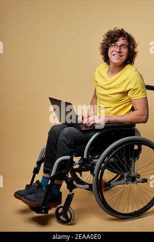 homme handicapé étudiant se préparant à l'examen avec un ordinateur portable, assis sur un fauteuil roulant isolé en studio. portrait. éducation en ligne pour les personnes handicapées Banque D'Images