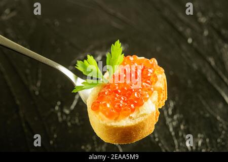 Tranche de pain frais blanc avec beurre et caviar rouge sur la fourchette, sur le fond noir de la vue rapprochée. Banque D'Images