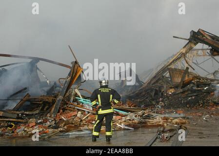 Les pompiers travaillent dans les ruines d'un entrepôt textile chinois qui a été incendié la 12e nuit des émeutes dans la banlieue parisienne du Bourget, en France, le 5 novembre 2005. De petits groupes mobiles de jeunes ont incendié des centaines de voitures supplémentaires et les violences et les attaques incendiaires qui ont secoué la banlieue de la capitale pendant une semaine se sont répandues dans d'autres villes françaises. Photo de Mehdi Taamallah/ABACAPRESS.COM Banque D'Images