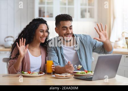Un couple arabe fait un appel vidéo sur un ordinateur portable dans la cuisine pendant que prendre le petit déjeuner Banque D'Images