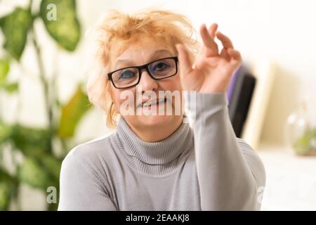 Souriante d'âge moyen mûr femme grise à cheveux regardant la caméra, heureux vieux posant à la maison à l'intérieur, positif femme célibataire senior retraité assis sur un canapé Banque D'Images