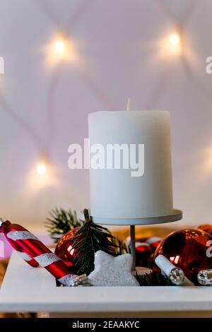 Arrangement de l'Avent, bougie blanche, ambiance romantique avec des lumières de fées, canne à sucre et boules d'arbre de Noël en rouge et blanc Banque D'Images