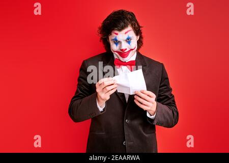 homme magicien effectuant un tour avec les mains isolées sur fond rouge, avec coloré halloween maquillage sur le visage Banque D'Images