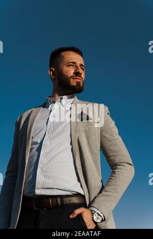 Bel homme arabe barbu dans des lunettes de soleil sur fond bleu ciel. Homme d'affaires musulman confiant. L'homme arabe a pleuré dans un manteau gris Banque D'Images