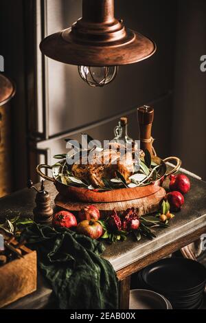 Poulet rôti entier pour les vacances d'hiver dîner festif dans un plat à rôtir en cuivre avec épices, herbes et fruits frais sur un comptoir de cuisine en béton. Concept de cuisine de Noël ou de Thanksgiving Banque D'Images