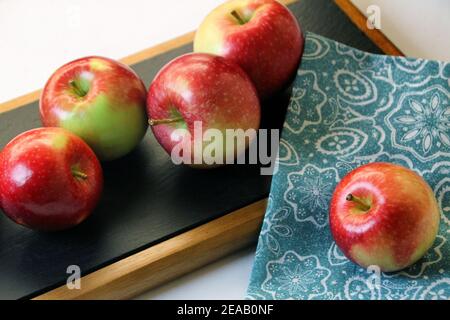 Quatre pommes Fuji rouges sont regroupées sur un plateau de service noir et une autre est placée sur une serviette bleue. Banque D'Images