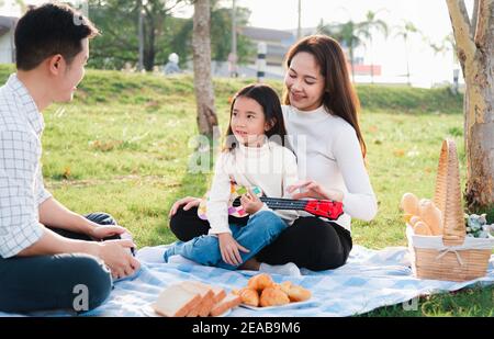 Joyeux père de famille asiatique jeune, mère et enfants s'amuser et profiter de l'extérieur ensemble assis sur la fête de l'herbe avec jouer Ukulele pendant un Banque D'Images